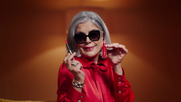 Zeenat Aman, dressed in a bold red outfit and sunglasses, poses confidently while holding a lipstick in each hand. The image exudes elegance and charm as part of a Hindustan Unilever beauty campaign.