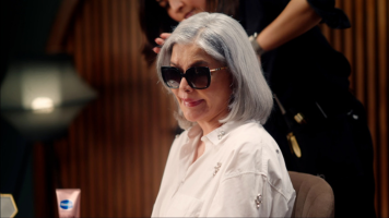 Zeenat Aman, wearing sunglasses and a white shirt, sits confidently while getting her hair styled. The image is part of a Hindustan Unilever campaign, reflecting elegance and timeless beauty.