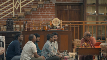 Four individuals seated, attentively listening to a person at a table in a room with eclectic decor.