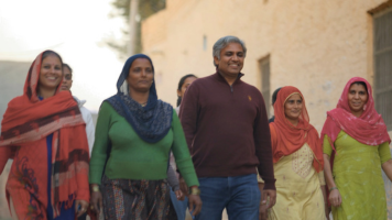 Group of people walking down a village street, dressed in colorful traditional clothing.